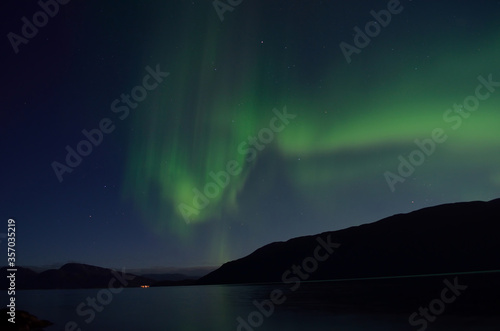 beautiful aurora borealis dancing over mountain and fjord landscape on late autumn night in northern Norway