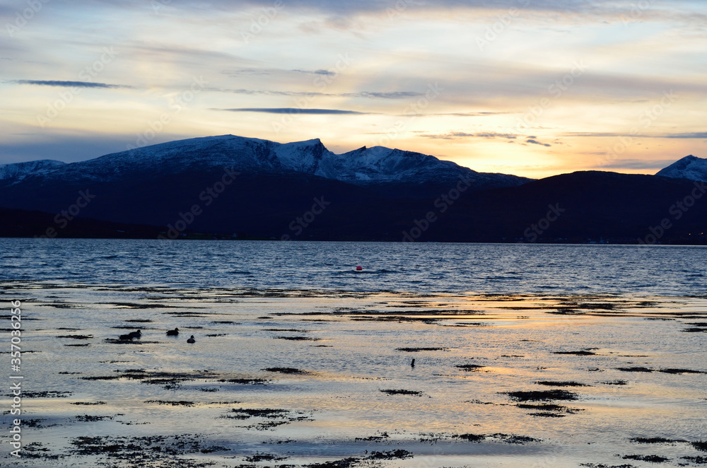 beautiful sunset over snowy mountain range and calm blue fjord