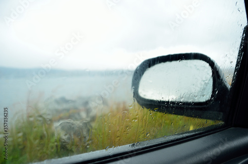 rain water sliding down car side window with mirror in the background