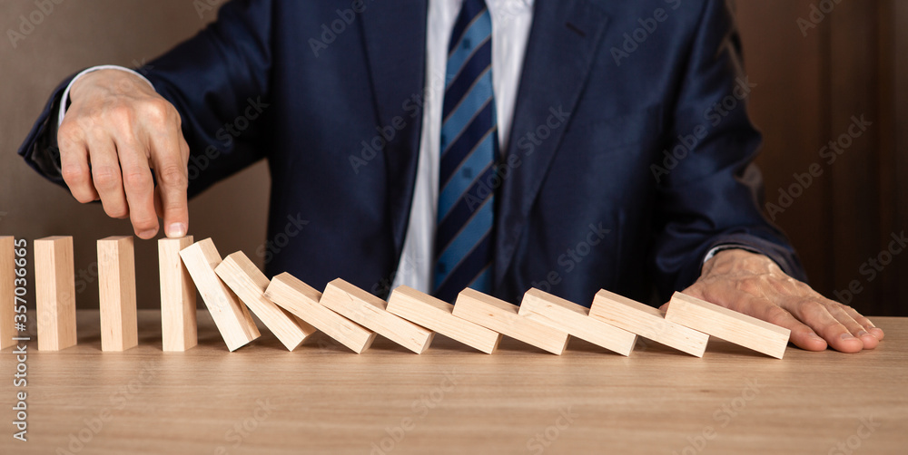 Businessman hand Stopping Falling wooden Dominoes effect from continuous toppled or risk, strategy and successful intervention concept for business.