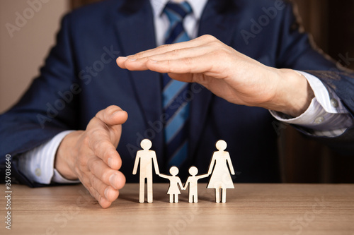 A man in a suit holds hands in the shape of a house over the family. Insurance concept.