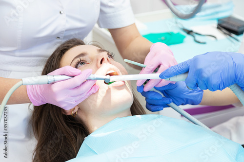 Dentist making teeth cleaning, treating and canal filling. assistant spaying mouth, using saliva ejector
