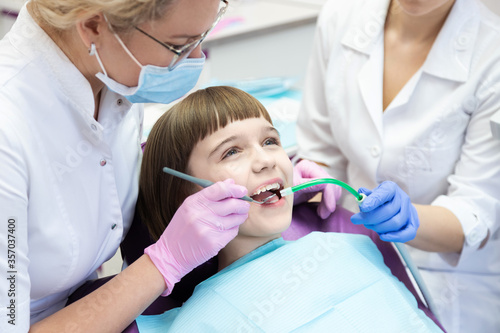 Dentist and assistant examining kid mouth with dentistry equipment instrument. 