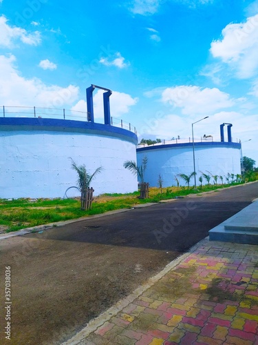 sewage water treatment plant tank or waste water recycle tank under blue sky. Road also see in the picture and palm trees are planted in road side