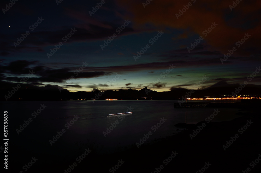 faint aurora borealis over mountain and calm fjord at sunset
