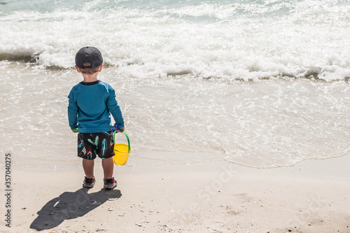 toddler playing on the beach with bucket of sand  photo