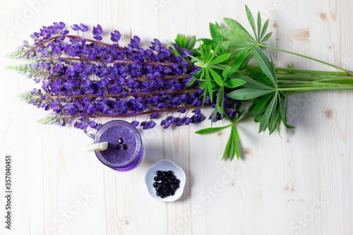 Flat lay on glass of fresh banana and blueberry smoothie and purple lupine flowers on wooden table with copy space photo