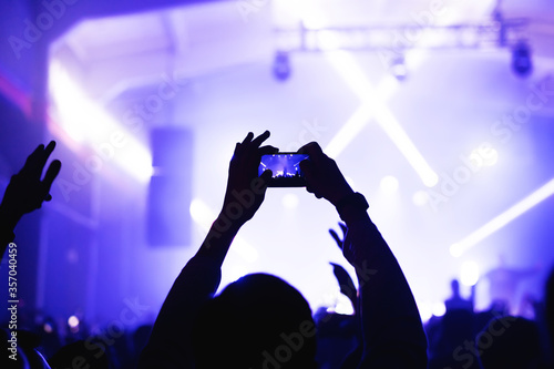The atmosphere of a cool music festival with a light-flooded stage and hands from the crowd with a smartphone. silhouette of a musician at a concert