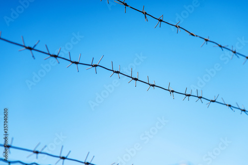 three rows of barbed wire with spikes over a fence against a blue sky. protection of private property and protected object. prison. aviary
