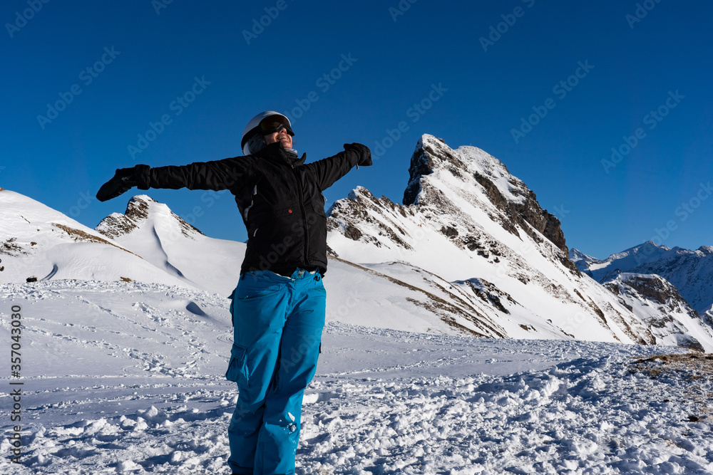 Girl enjoying winter sunbeams with open arms at top of the mountain range.
