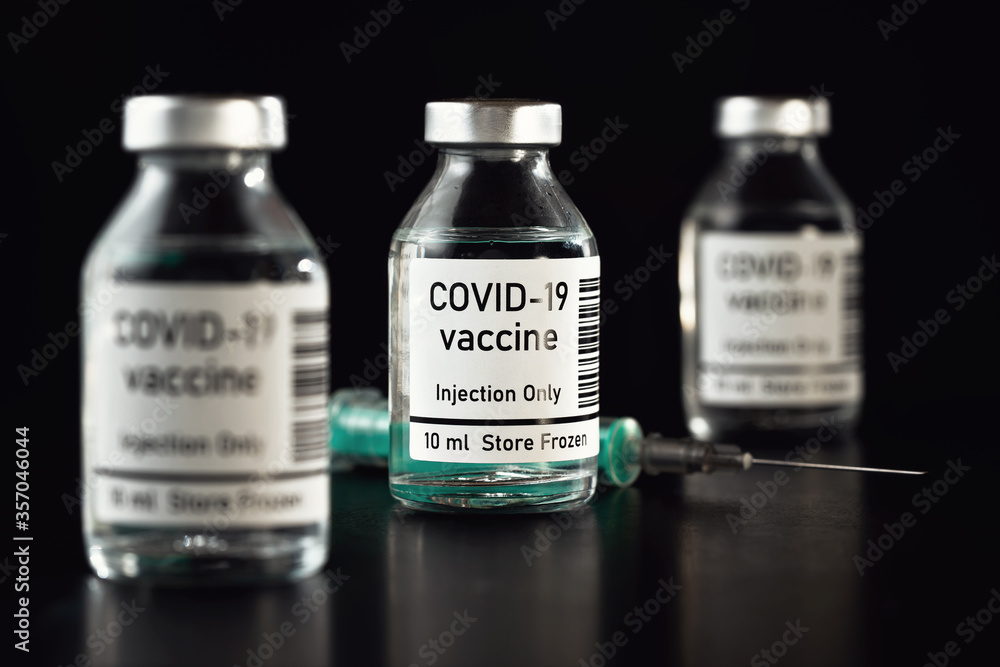 Coronavirus Covid-19 vaccine concept - three glass vials on black table, hypodermic syringe needle near, closeup detail (label own design - dummy data and barcode, not real product) Coronavirus Covid-19 vaccine concept - three glass vials on black table, hypodermic syringe needle near, closeup detail (label own design - dummy data and barcode, not real product)