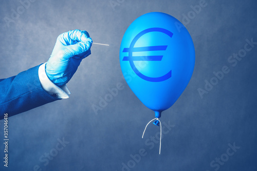 Euro currency symbol on blue balloon in coronavirus time. Man hold needle directed to air balloon. Concept of finance risk.
