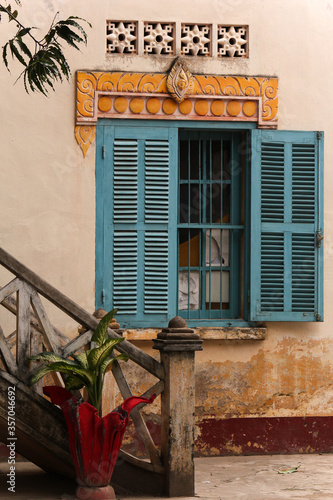 Old window with blue wooden blinds and an ancient stairway of a monks residence in a wat in Siamese Lao PDR, Southeast Asia