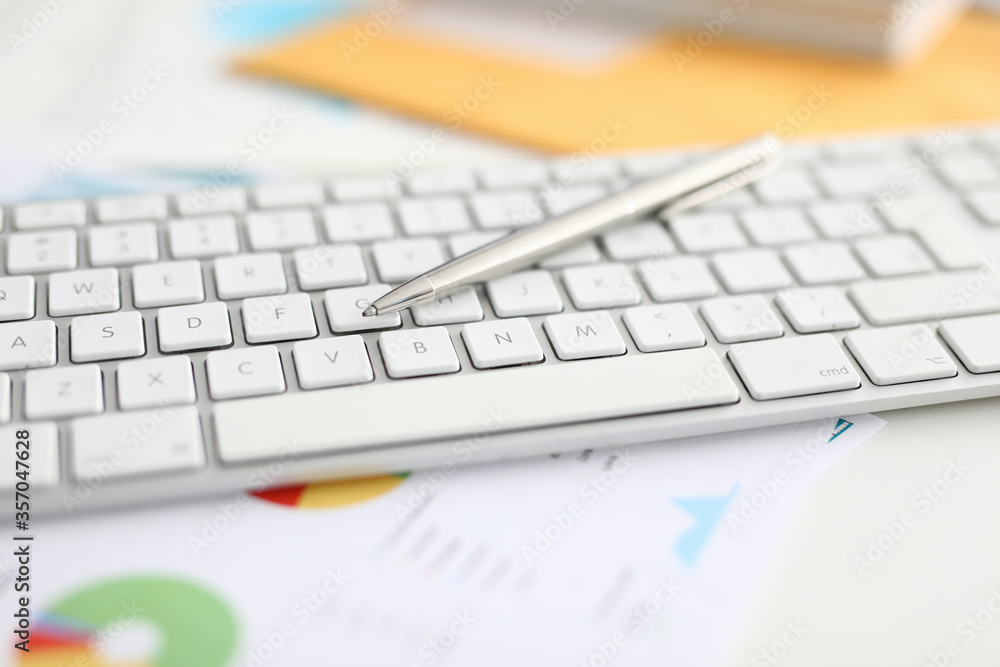 Close-up of white modern laptop keyboard on table. Silver pen for writing. Paper with chart in office. Executive manager desktop. Business cabinet and personal stuff concept Close-up of white modern laptop keyboard on table. Silver pen for writing. Paper with chart in office. Executive manager desktop. Business cabinet and personal stuff concept