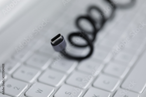 Close-up of black cable for connecting to device lies on white computer keyboard. Laptop accessories. Usb input for tablet. Fast charger. Modern technology and pc concept