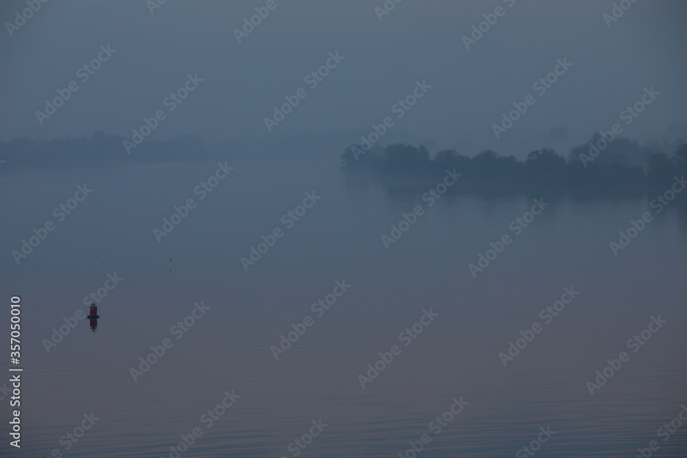 A single signal buoy on the water in the early morning in a blue fog.Russia A single signal buoy on the water in the early morning in a blue fog.Russia