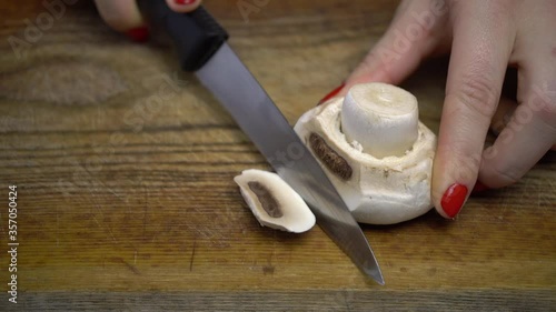 Champignon lies on blackboard, girl with red manicure cuts mushroom with slices