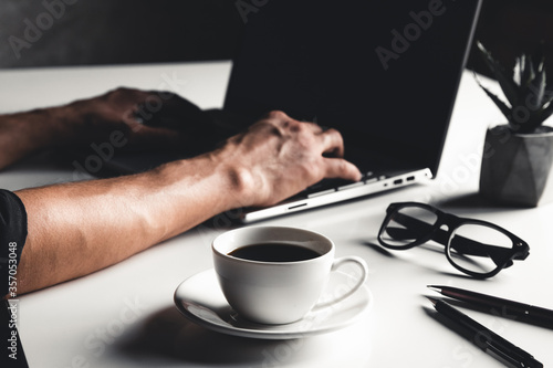 A man types on a laptop  business concept  glasses  a cup of coffee and a pen on a gray background.