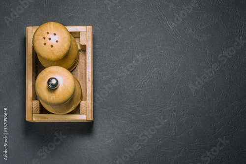 Wooden salt shaker and pepper shaker in box on the left side on black surface