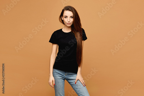 Young smiling woman with slim perfect body in a black t-shirt at the beige background, isolated. Sale advertisement mockup