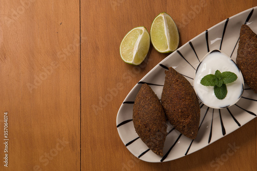 Close up fried kibbeh yogurt sauce served on a white plate photo