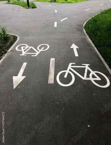 Bike Lane. The bike signs on the asphalt are painted with white paint. Two bike path signs pointing in opposite directions are indicated by white arrows. White road markings visible