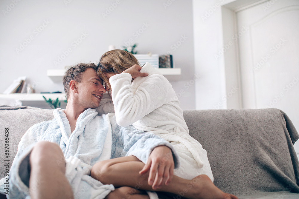 Cute couple in love in the weekend morning. They are hugging on the sofa indoors at home,