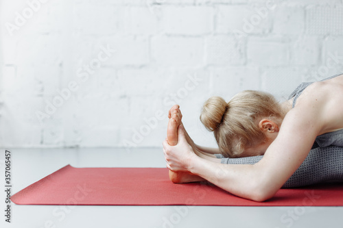 woman in triang mukhaikapada pashchimottanasana yoga position. Young attractive woman practicing yoga, working out, wearing sportswear, pants and top, indoor full length, yoga studio photo