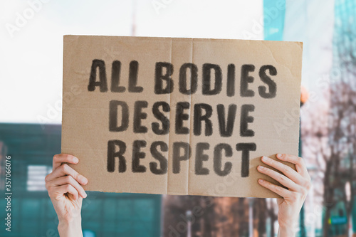 Fototapeta The phrase  All bodies deserve respect  on a banner in men's hand with blurred background