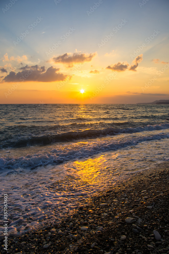 Amazing sea sunset on the pebble beach, the sun, waves, clouds