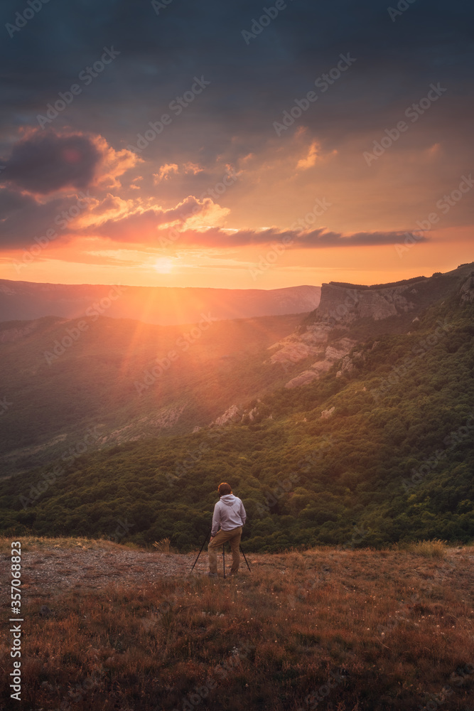 Photographer with a tripod photographs a mountain landscape at sunset. Hobby, landscape photography, backstage. Copy space.