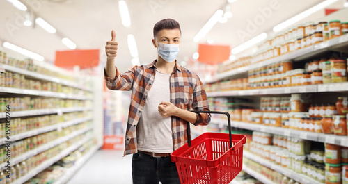 Guy in a supermarket with a protective mask and a shopping basket showing thumbs up