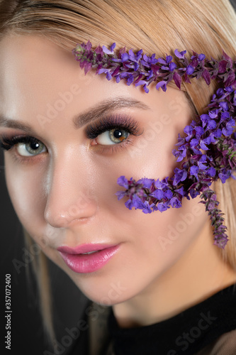 Fototapeta Naklejka Na Ścianę i Meble -  Woman's blue green eye with pupil heterochromia with beautiful make-up and thick eyebrows. Near her are beautiful blooming spring flowers. Looking at the camera. Professional makeup and cosmetology.