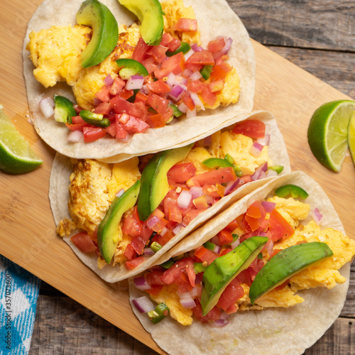 Breakfast egg tacos with flour tortilla and fresh sauce on wooden background