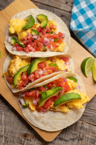 Breakfast egg tacos with flour tortilla and fresh sauce on wooden background