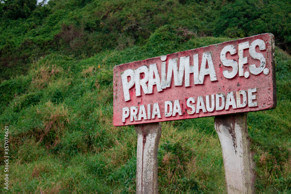 Praia da Saudades, placa de boas vindas, em vermelho, fundo verde, com a natureza local