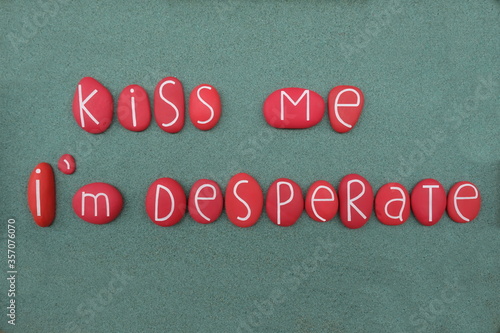 Kiss me, I'm desperate, funny slogan composed with red colored stone letters over green sand photo