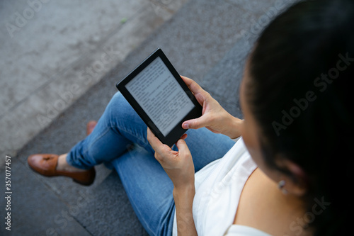young latin woman reading an ebook on digital tablet device. Focus on the ebook.