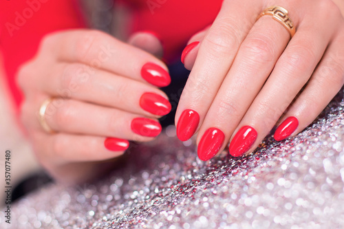 Close up view of female hands with luxury and glamour manicure  nails with red gel polish on sparkling background