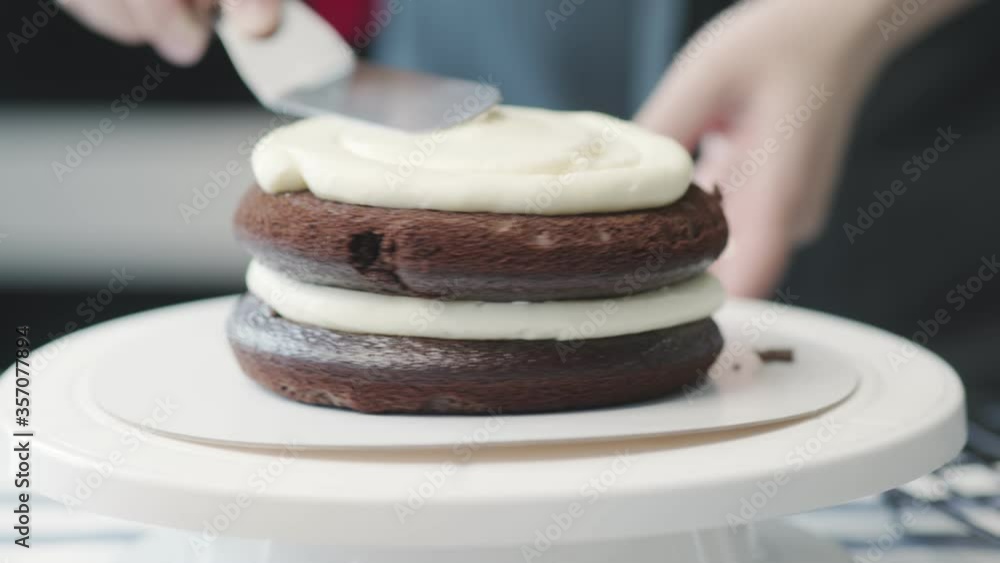 Professional chef is cooking cake. Close up of housewife uses metal spatula aligns white cream on chocolate cake Professional chef is cooking cake. Close up of housewife uses metal spatula aligns white cream on chocolate cake