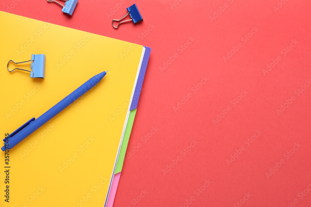 Yellow notebook with pen and binder clips on red background, flat lay. Space for text Yellow notebook with pen and binder clips on red background, flat lay. Space for text
