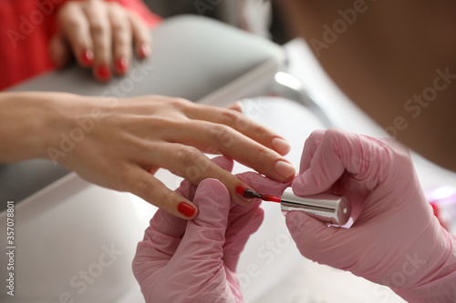 Professional manicurist applying polish on client s nails in beauty salon  closeup