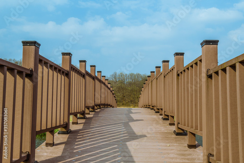 Closeup perspective of wooden footbridge with trees and partly cloudy blue sky in background.