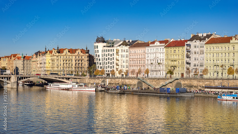 Apartment Buildings on the Vltava River Waterfront in Prague, a River with Boats and Walking Tourists