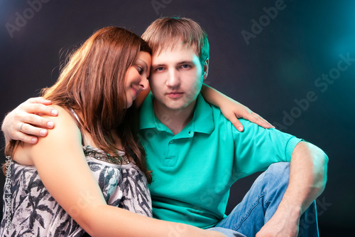 Family and Relationships Concepts. Portrait of Pregnant Woman Together with Her Husband Sitting Together Embraced. Against Black. photo