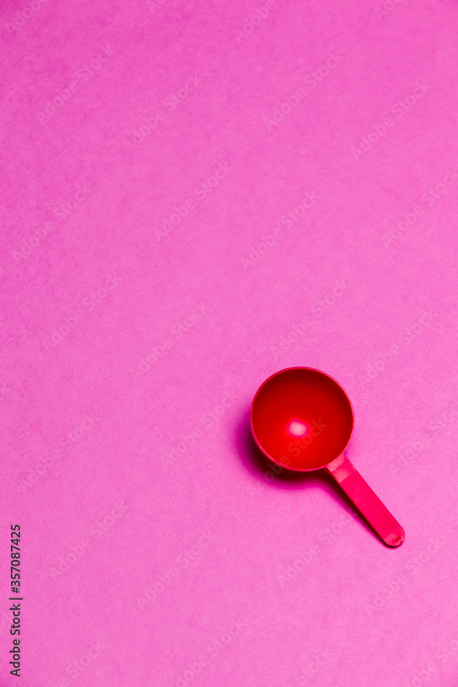 Red Plastic Round Spoon Placed Over Colorful Pink Background. Red Plastic Round Spoon Placed Over Colorful Pink Background.