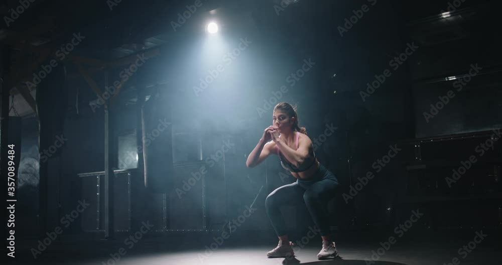 Young determined female athlete working out in gym in the evening, doing intensive sit-up squats, perfecting gym routine achieving goals 4k footage Young determined female athlete working out in gym in the evening, doing intensive sit-up squats, perfecting gym routine achieving goals 4k footage