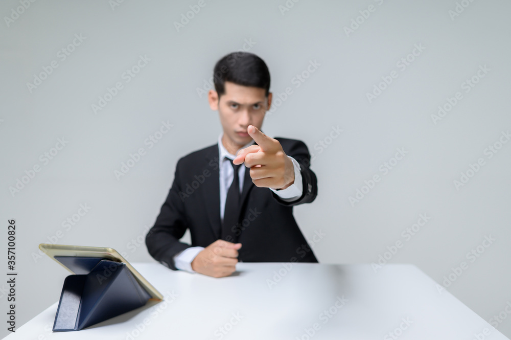 Handsome young businessman sitting with a finger pointing forward at the table. Handsome man with tablet and table isolated on white background. Handsome young businessman sitting with a finger pointing forward at the table. Handsome man with tablet and table isolated on white background.