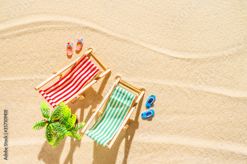 Aerial view of two deck chair, sunbed, lounge, flip flops, palm tree on sandy beach. Summer and travel concept. Minimalism