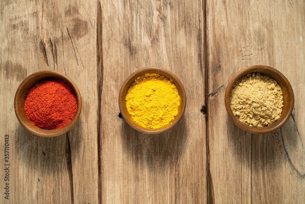 Three bright spices (cayenne, turmeric, ginger) in a wooden bowl on a table. Top view
